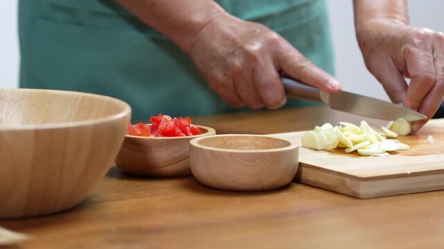 Hands chopping fresh garlic with a kitchen knife for homemade cooking.
