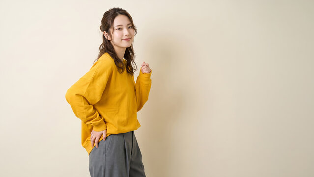 明るい色のトップスとグレーのパンツを着てポーズをとる笑顔の女性