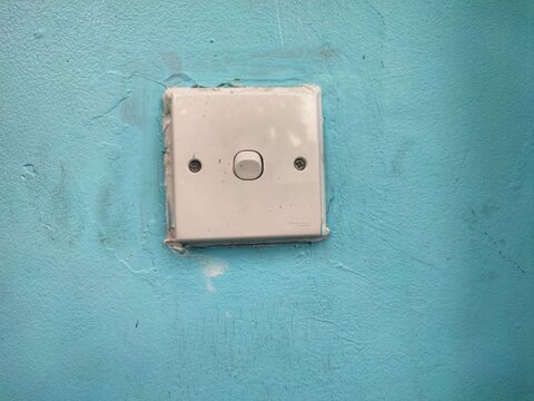 A single white light switch mounted on a textured light blue wall.