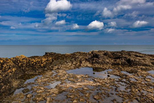 Rocky shoreline and rock pools at Penmon Point on the Isle of Anglesey under a blue sky with scattered clouds