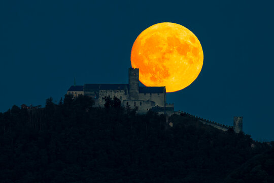 Huge full moon rising behind medieval Bezděz Castle during blue hour in the Czech Republic, creating a dramatic telephoto night landscape.