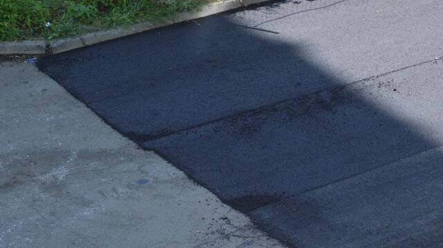 Freshly laid dark asphalt pavement on a section of a city road close up. New high quality road surface is ready for operation after completion of construction works