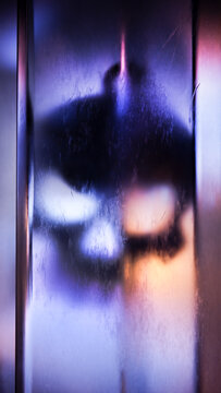 Dark blurred form behind luminous vertical glass and reflections.