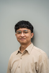 Obraz premium A smiling man with glasses poses for a portrait against a light gray background.