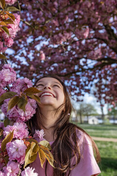 Happy girl looking up at blooming pink cherry blossoms in spring