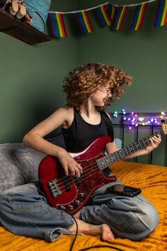 Teenage girl plays electric bass on bed in her bedroom