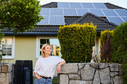 Smiling woman standing by fence outside house with solar panels