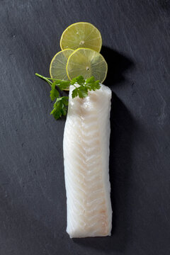 Fish fillet of codfish with slices of lime on grey background