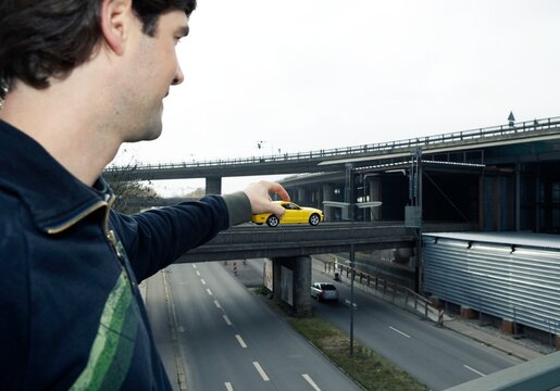Holding a yellow toy car over a city highway in forced perspective