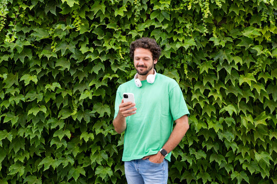 A man uses a smartphone outdoors against a green ivy wall