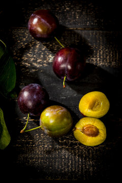 Whole and sliced plums on dark wood