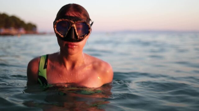 Woman in snorkeling mask takes a deep breath at the sea surface then dives underwater to explore coastal water during a summer evening swim in warm golden sunset sunlight