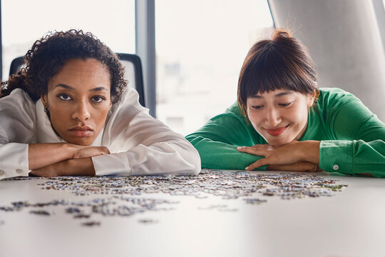 Female colleagues solve a jigsaw puzzle in a London office boardroom