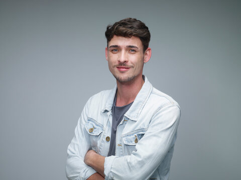 Portrait of smiling young man with crossed arms in front of grey background