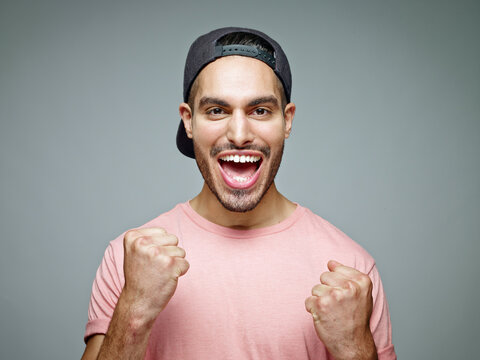 Portrait of man with baseball cap screaming for joy in front of grey background