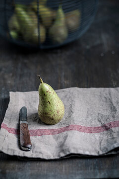 Pear with water trops and knife on kitchen towel, basket with pears