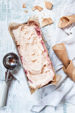 Vanilla icecream with fruit swirl in loaf pan and ice-cream cones, ice cream scoop