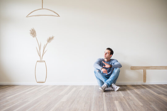 Young man in new home sitting on floor thinking about interior decoration