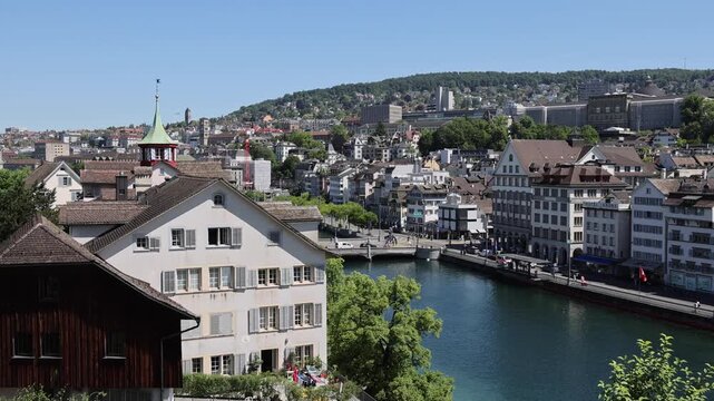 View of historic buildings along the Limmat river with lush trees and urban architecture in Zurich, Zurich, Switzerland.