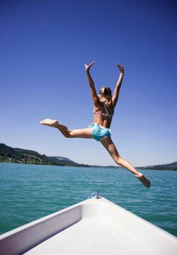 Teenage girl (13-15) jumping from boat into water, rear view