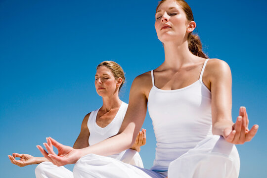 Mother and daughter sitting in lotus position on beach, low angle view