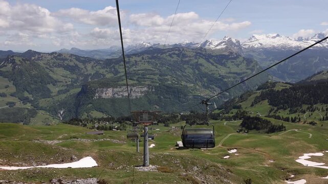 View of Fronalpstock mountain peak with lush green alpine meadows, patches of snow, and a chairlift system in the foreground in Morschach, Schwyz, Switzerland.