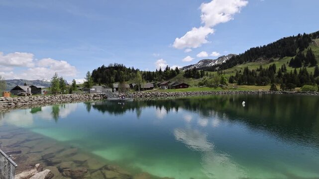 View of Stoos lake with clear water and surrounding green mountains under a blue sky in Schwyz, Schwyz, Switzerland.