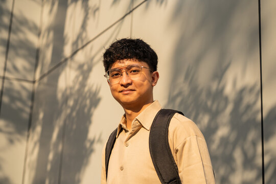 A young man stands confidently outdoors with a backpack, surrounded by trees and nature.