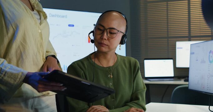 Togetherness and teamwork in a busy call center. Two Asian female employees wearing earphones with microphones, communicating data and providing excellent business service.