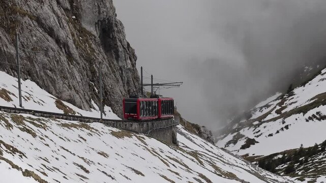 View of the red cogwheel train ascending the steep, snow-covered slopes of Mount Pilatus in Alpnach, Obwalden, Switzerland.