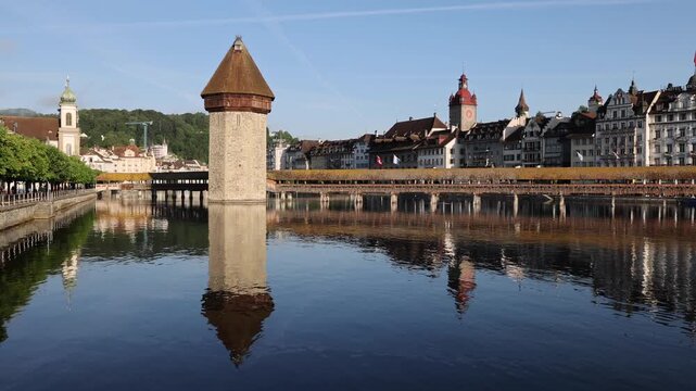View of the historic wooden Chapel Bridge and its iconic octagonal Water Tower reflecting in the calm Reuss River, with the city skyline in Lucerne, Lucerne, Switzerland.
