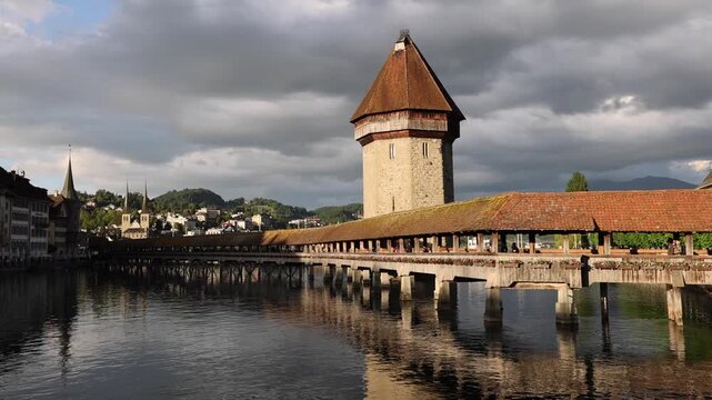 View of the historic Chapel Bridge and Wasserturm spanning the Reuss River under a dramatic cloudy sky in Lucerne, Lucerne, Switzerland.