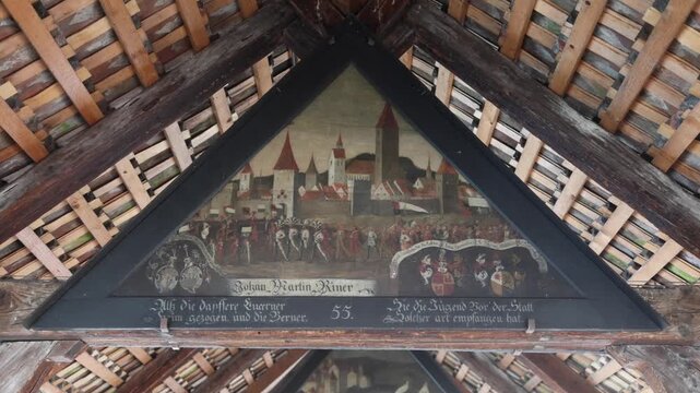 View of a historic triangular painting depicting a medieval city scene with coats of arms inside the wooden roof structure of the Chapel Bridge in Lucerne, Lucerne, Switzerland.