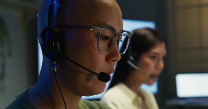 Two confident Asian businesswomen working as customer service representatives. Diverse colleagues using headsets and computers to provide client support and advice in the office.