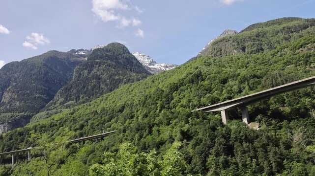 View of the Gotthard Panorama Express train route passing through lush green mountains and concrete viaducts in Lugano, Ticino, Switzerland.