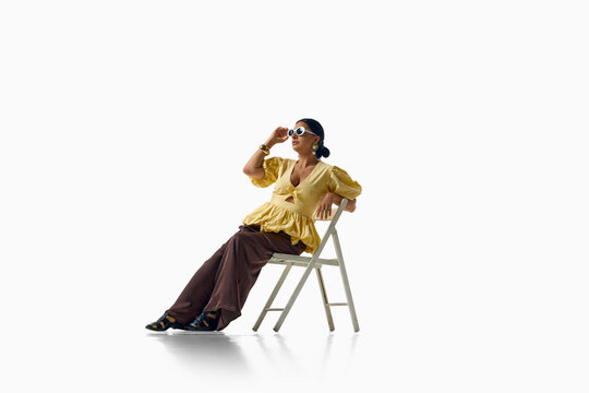 Stylish woman relaxes on chair in yellow blouse and wide trousers. Concept of confident personal style, comfortable fashion, statement clothing and modern femininity.