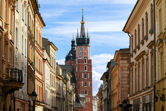 A picturesque view down a cobblestone street in Krakow, Poland, framed by colorful historic buildings towards a prominent church tower