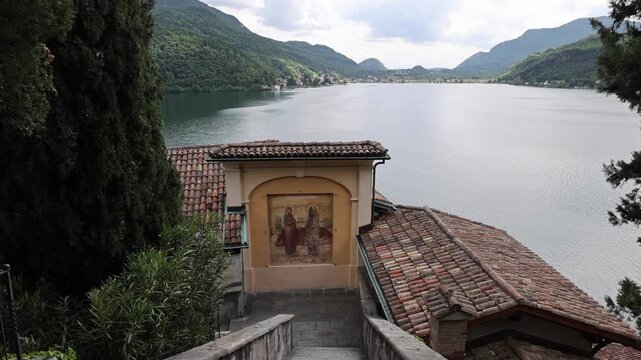 View of the historic stone stairs and religious fresco at the Chiesa di Santa Maria del Sasso overlooking Lake Lugano in Morcote, Ticino, Switzerland.