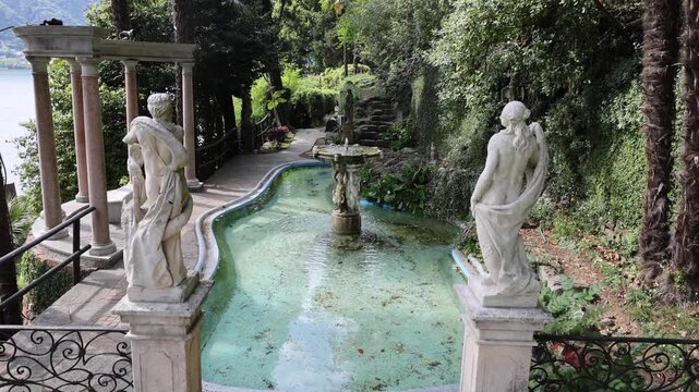 View of classical statues and a stone fountain in a lush garden setting overlooking the lake in Morcote, Ticino, Switzerland.