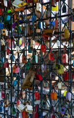 Fototapeta premium Hundreds of colorful love padlocks hang on a metal fence, symbolizing romance, commitment and lasting relationships. Popular urban tradition and tourist attraction with vintage locks.