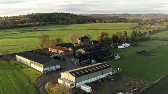 Aerial view of a traditional farmhouse and barn complex surrounded by green agricultural fields in the countryside during golden hour.