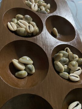 Traditional Southeast Asian wooden Mancala board game called Congklak with natural cowrie shells in round holes on a brown surface, showcasing cultural heritage and indoor leisure play.