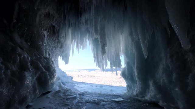 View of icicles hanging from the ceiling of a frozen ice cave overlooking the vast winter landscape of Lake Baikal in Khuzhir, Irkutsk Oblast, Russia.