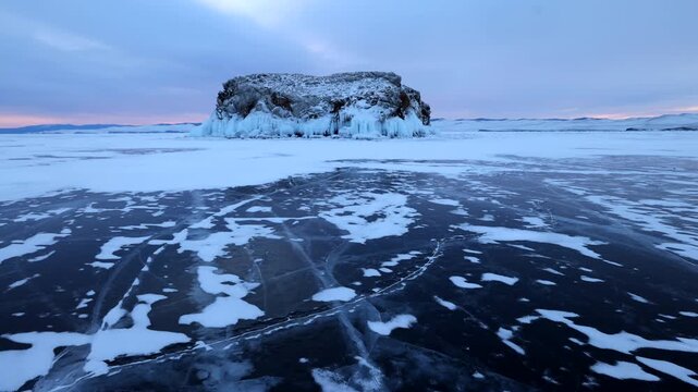 View of the frozen surface of Lake Baikal with a rocky island and snow-covered ice in Khuzhir, Irkutsk Oblast, Russia.