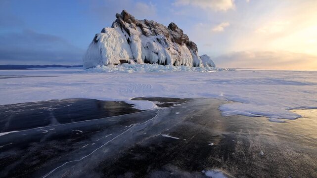 View of Lake Baikal ice formations with a rocky island surrounded by frozen water under golden hour light in Khuzhir, Irkutsk Oblast, Russia.
