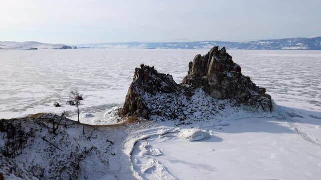View of the iconic Shamanka Rock on the frozen surface of Lake Baikal with snow-covered cliffs and winter landscape in Khuzhir, Irkutsk Oblast, Russia.