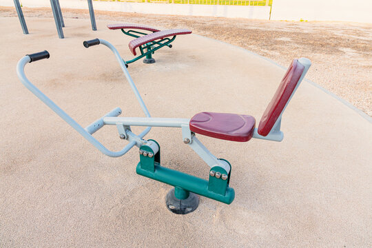 Outdoor park fitness area with modern outdoor gym equipment on sandseated rower, sit up bench, public access
