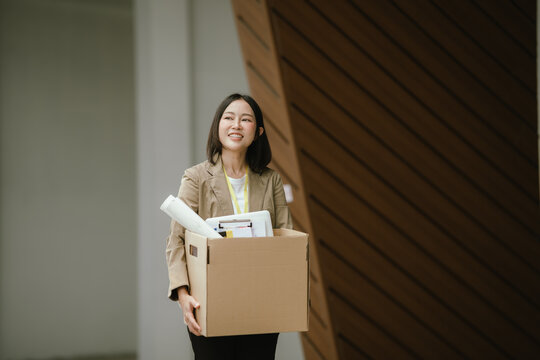 Happy female office worker carrying a cardboard box filled with personal belongings, representing job transition, career change, new opportunities, and a positive fresh start.
