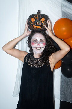 Woman with Halloween makeup holding pumpkin decoration on her head