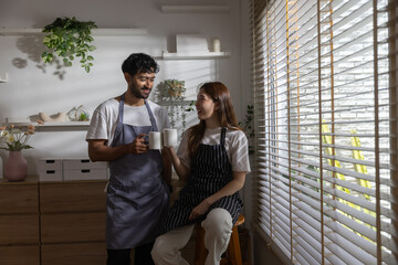 Obraz premium Happy couple enjoying coffee together by sunny kitchen window, smiling and sharing relaxing break from cooking that reflects connection, togetherness, positive home lifestyle.